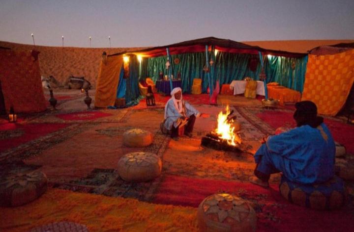 dos personas sentadas alrededor de un fuego en una tienda en Desert Berber Camp, en Merzouga
