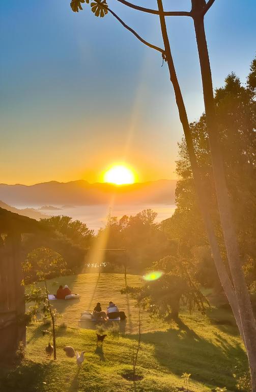 a group of people sitting in a field at sunset at Hospedaria Vida na Roça in São Bento do Sapucaí