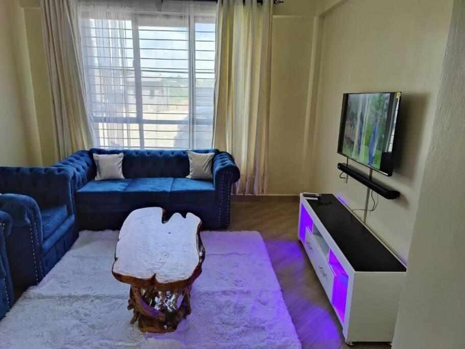 ein Wohnzimmer mit einem blauen Sofa und einem TV in der Unterkunft Mupa's Luxury Condo I in Nyahururu