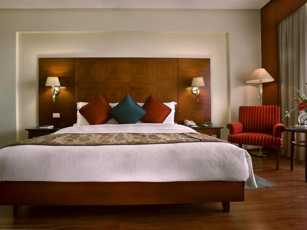 a bedroom with a large bed and a red chair at Glacee Stay Hotel Near Delhi Airport in New Delhi