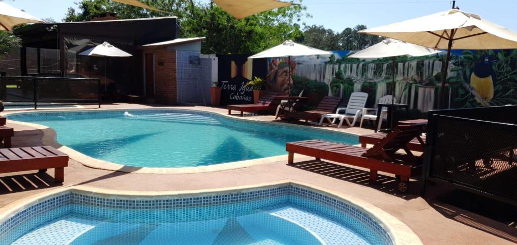 ein Pool mit Bänken und Sonnenschirmen neben in der Unterkunft Terra Iguazú Cabañas in Puerto Iguazú