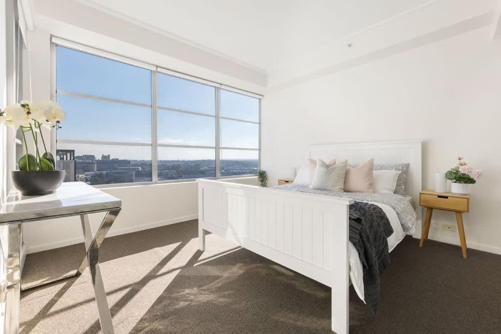 a white bedroom with a white bed and a large window at A Spacious 2BR Apt with an Amazing View Over Darling Harbour in Sydney