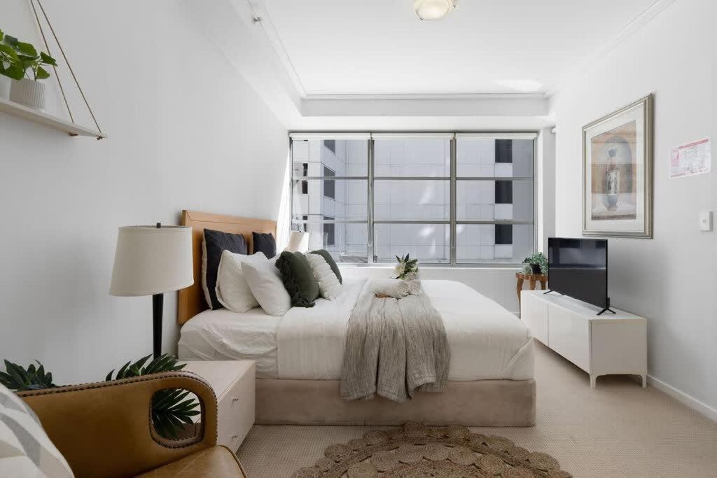 een witte slaapkamer met een bed en een raam bij A Comfy 2BR Apt for 7 Next to Darling Harbour in Sydney