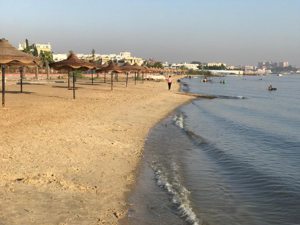 una spiaggia con ombrelloni di paglia e persone in acqua di Chalets and apartments Al-Nawras Village Ismailia a Ismailia