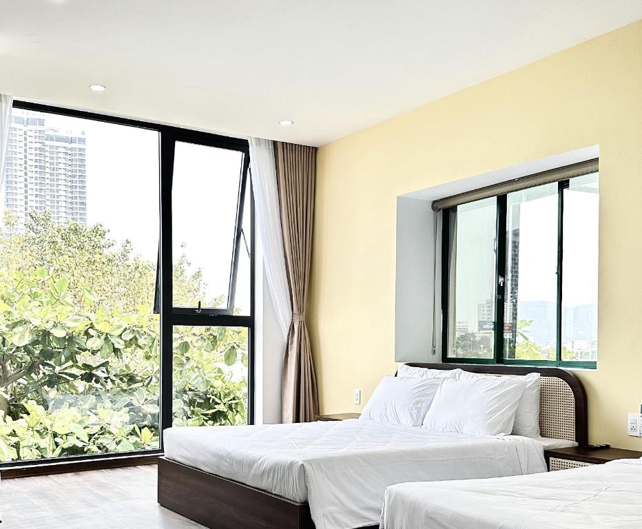 two beds in a room with large windows at Han Riverine Hotel & Cafeteria DaNang in Da Nang
