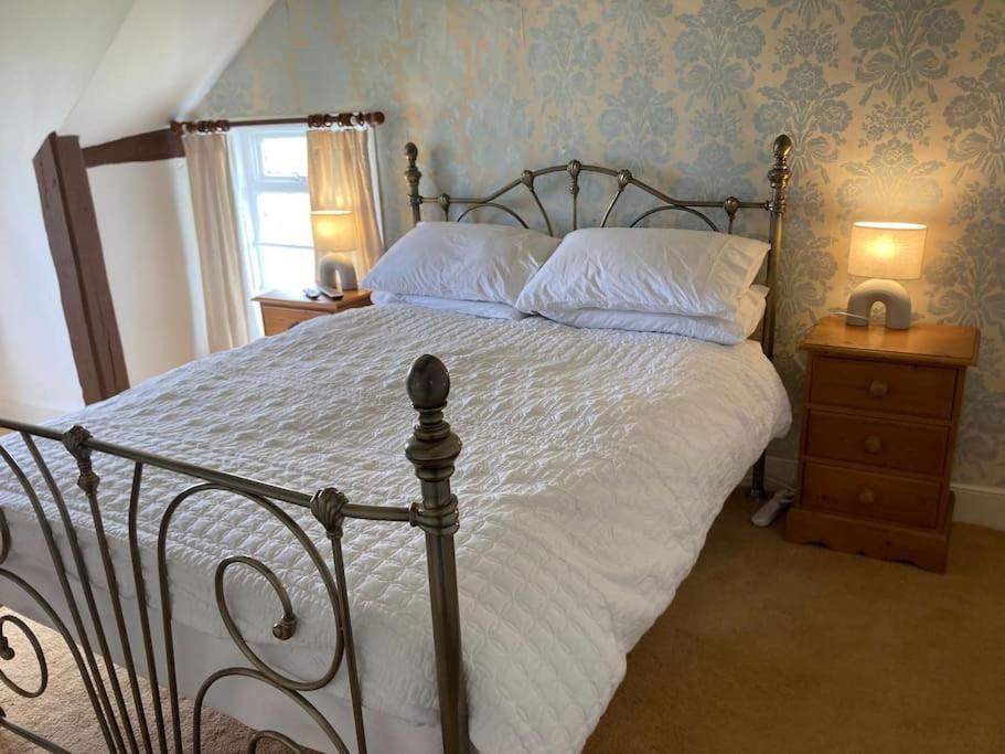 um quarto com uma cama grande com lençóis brancos e almofadas em Bryntirion Farmhouse Rooms (with bathroom) em Llanfair Caereinion