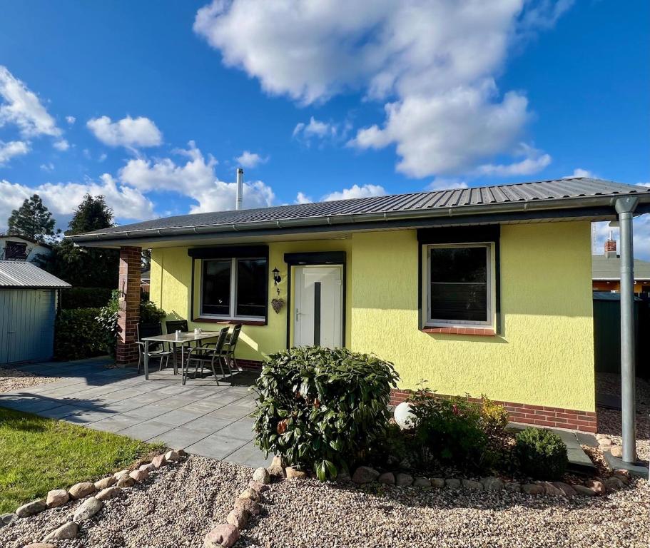 ein gelbes Haus mit einer Terrasse und einem Tisch in der Unterkunft Ferienbungalow Muranko am Kiessee in Krugsdorf