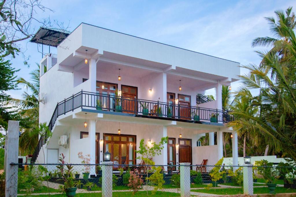 a white house with a balcony and palm trees at My Resort Yala in Tissamaharama