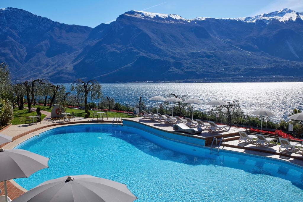 a swimming pool with chairs and umbrellas next to a lake at Hotel Atilius in Limone sul Garda