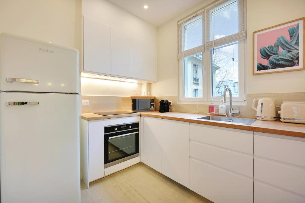 a white kitchen with a refrigerator and a sink at Comfy Suite by Les Maisons de Charloc Homes in Boulogne-Billancourt