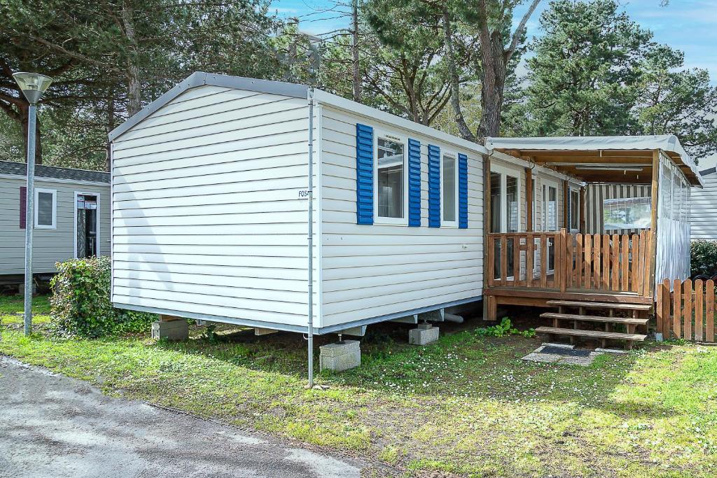 Cette petite maison blanche dispose de fenêtres bleues et d'une terrasse couverte. dans l'établissement Mobilhome au bois masson, à Saint-Jean-de-Monts