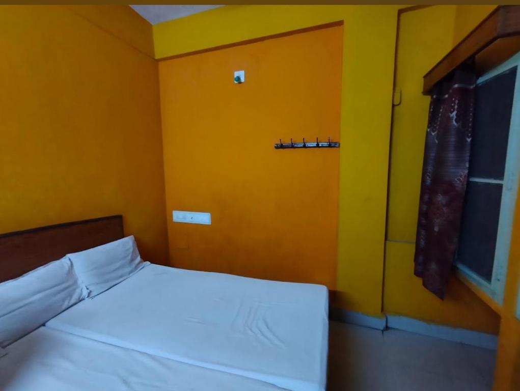 1 dormitorio con cama blanca y pared amarilla en Ganesh Lodge en Tirupati