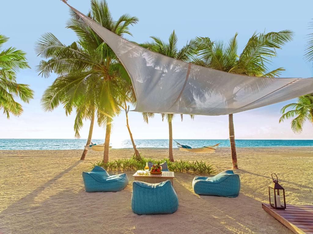 een strand met stoelen en een tafel en palmbomen bij One&Only Reethi Rah in Reethi Rah