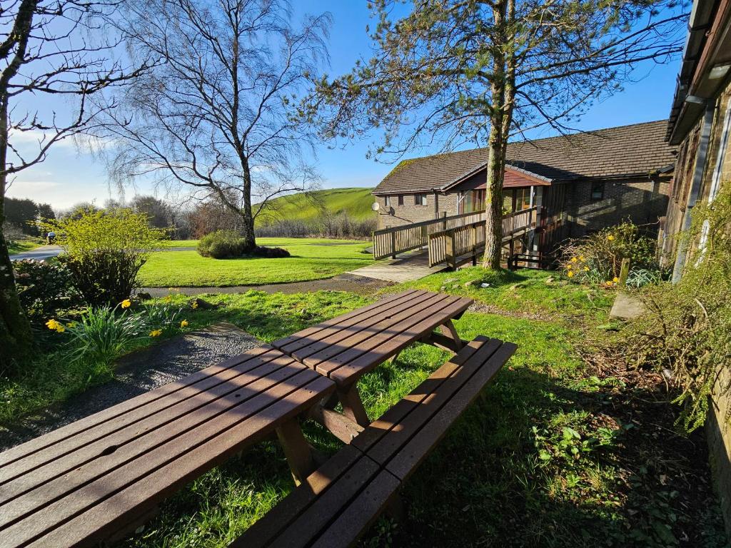 un banc en bois assis dans l'herbe devant une maison dans l'établissement Stunning Rural 72 bed bunkhouse 21 Bedrooms, à Elerch