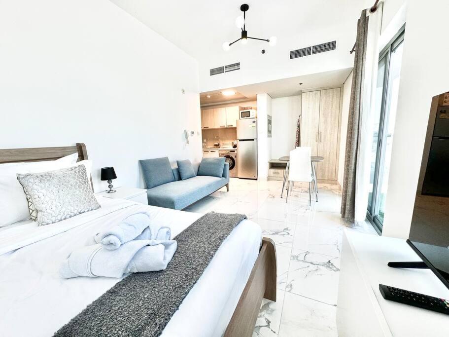 a white bedroom with a large bed and a living room at Mag 5 Spacious studio apartment in Dubai