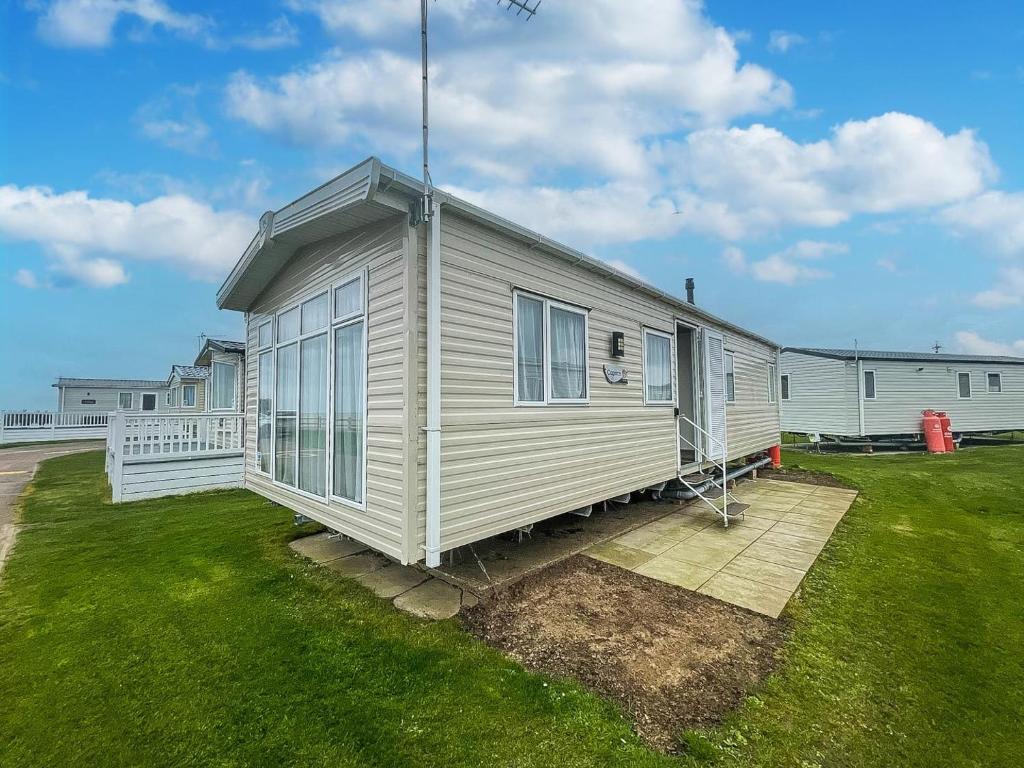 a small white house on a grass field at Modern 6 Berth Caravan With Free Wifi Nearby Pakefield Beach Ref 68028cr in Lowestoft