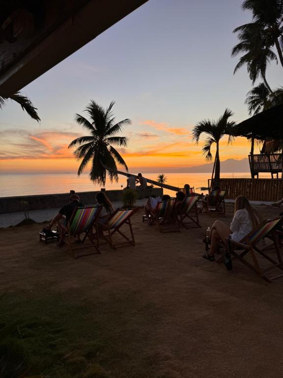 people sitting in chairs on the beach at sunset at Room-Cola Inn in Siquijor
