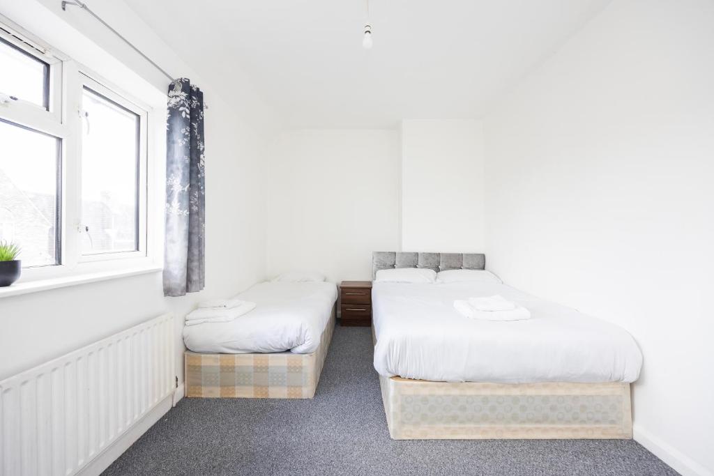 2 Betten in einem weißen Zimmer mit Fenster in der Unterkunft DAGENHAM 3 BEDROOMS2BATHS in Dagenham
