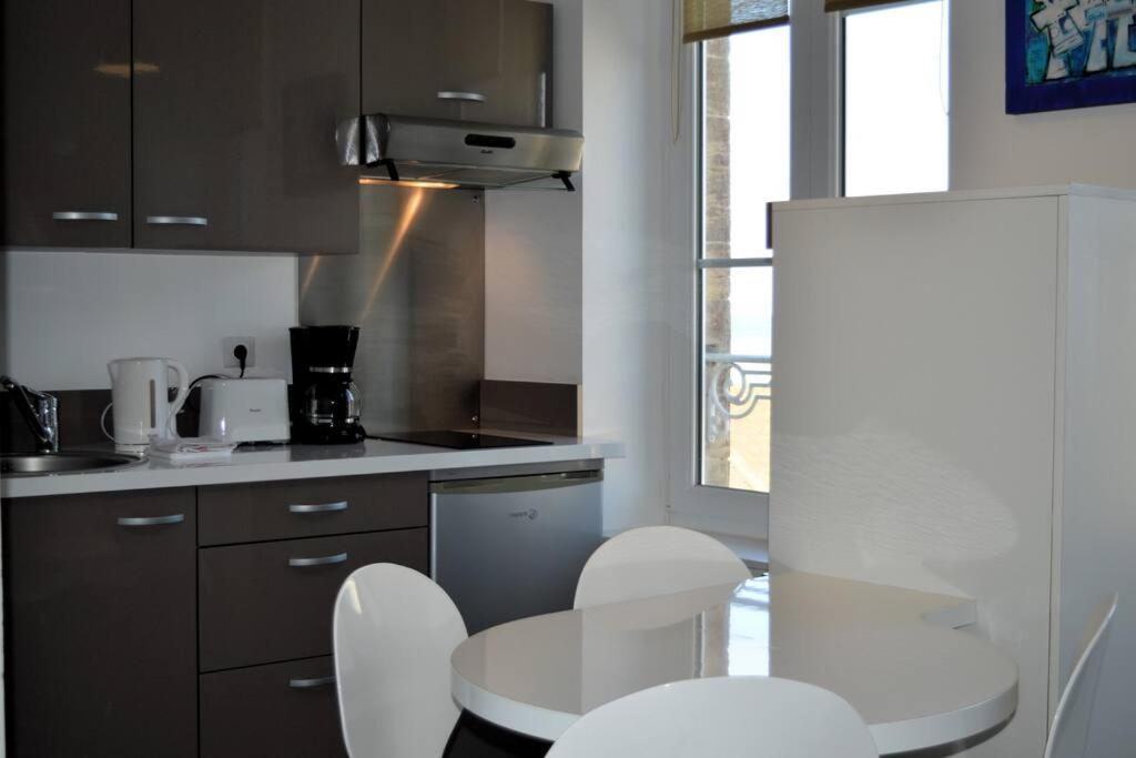 a kitchen with a table and some white chairs at Le Joffre - studio sur la digue en centre ville in Arromanches-les-Bains
