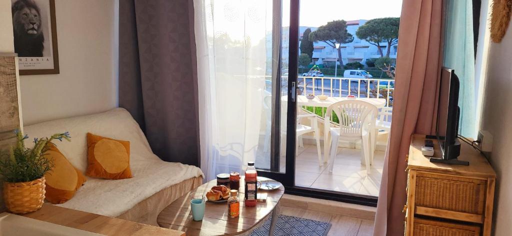 ein Wohnzimmer mit einem Sofa, einem TV und einem Balkon in der Unterkunft Terrasses 2 - Plage et commerces à 400 m in Le Grau-du-Roi