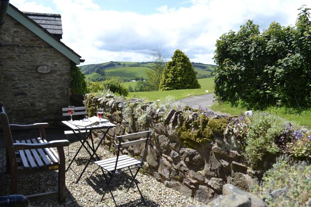 a table and chairs in front of a stone wall at Dunkery Cottage Wheddon Cross in Minehead