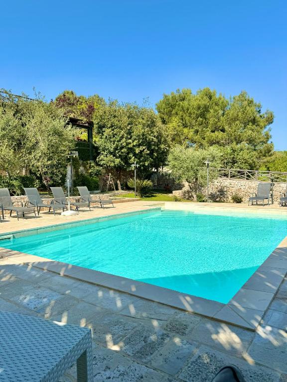 basen z niebieską wodą, krzesłami i drzewami w obiekcie Trulli Bosco Selva w Alberobello