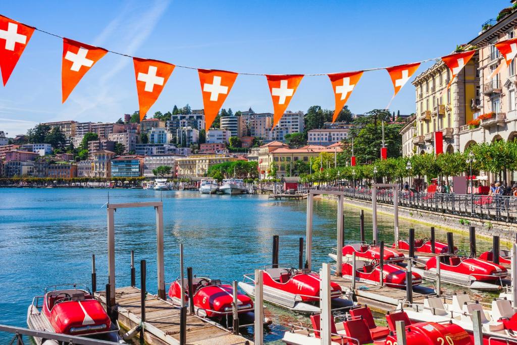 a bunch of boats are docked on a river with flags at Star of Lugano - Happy Rentals in Lugano