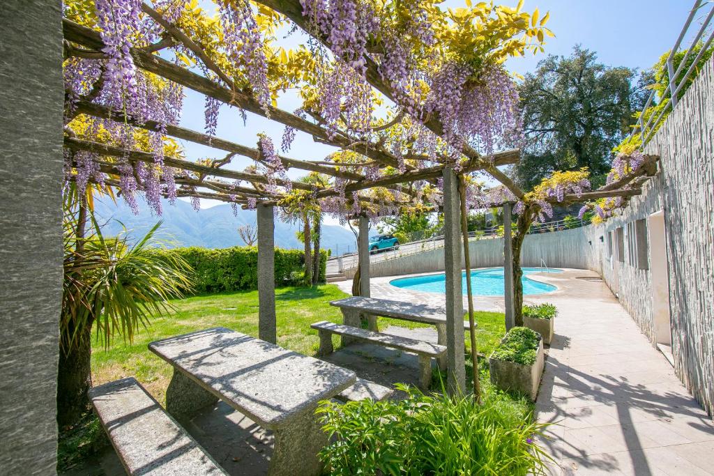 a picnic table and bench under a pergola with purple flowers at Casa Monti Belvedere - Happy Rentals in Locarno
