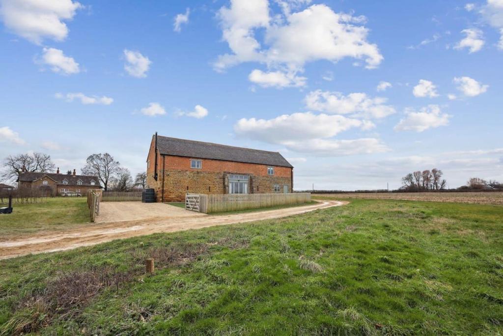 a brick barn in a field with a dirt road at Sophie's Barn - Hot Tub Packages Available in Market Harborough