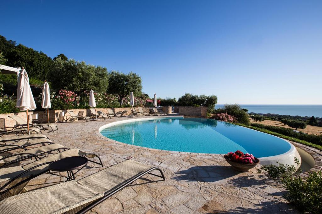 a swimming pool with chairs and umbrellas and the ocean at Pamperduto Country Resort in Porto Potenza Picena