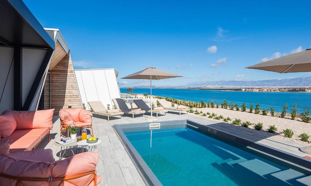 a swimming pool with chairs and umbrellas next to the water at Aminess Avalona Glamping Villas & Mobile Homes in Povljana