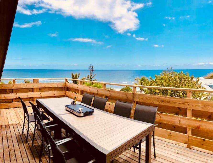 a wooden deck with a table and chairs and the ocean at Grand Appartement Mer - Pétrel 1 in Trois Bassins