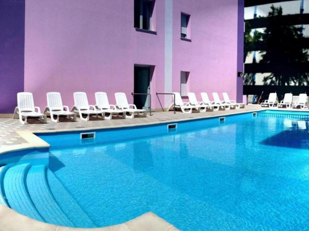 einem Pool mit weißen Stühlen und einem lila Gebäude in der Unterkunft Comfortable apartment with terrace - Beahost in Bibione