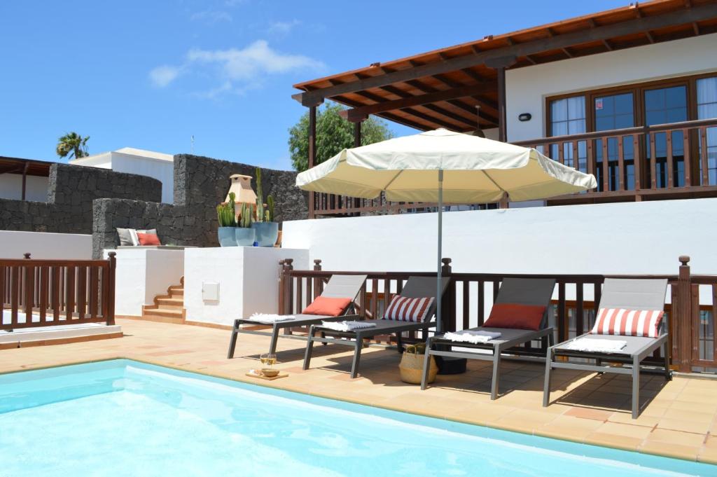 eine Terrasse mit 2 Stühlen und einem Sonnenschirm neben einem Pool in der Unterkunft Villa Tegala in Playa Blanca