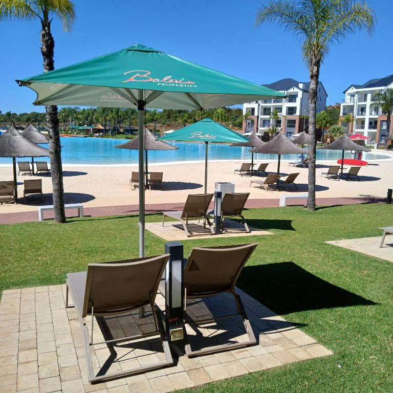 een tafel en stoelen onder een parasol naast een zwembad bij The Luxe Marvelous Apartment in Pretoria
