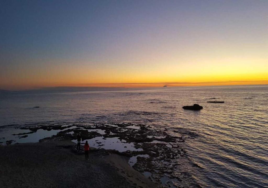 a sunset over the ocean with people standing on the beach at Uno Spettacolo Della Natura, Modern Style in San Lucido