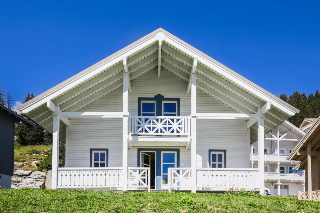 une maison blanche avec des portes bleues et une terrasse couverte dans l'établissement Les Chalets de Flaine Hameau - maeva Home - Chalet 5 Pièces 8 Personnes - Con 61, à Flaine