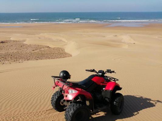 a red motorcycle parked in the sand on the beach at sidi kaouki ayt karoum in Sidi Kaouki
