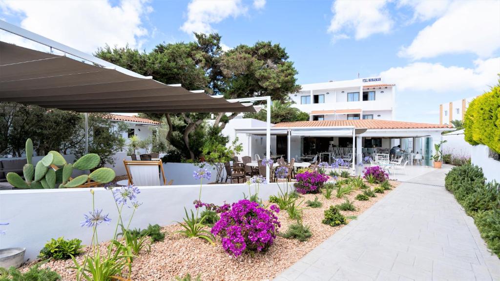 um jardim com flores roxas e uma parede branca em Hotel Rosamar - Emar Hotels em Es Pujols