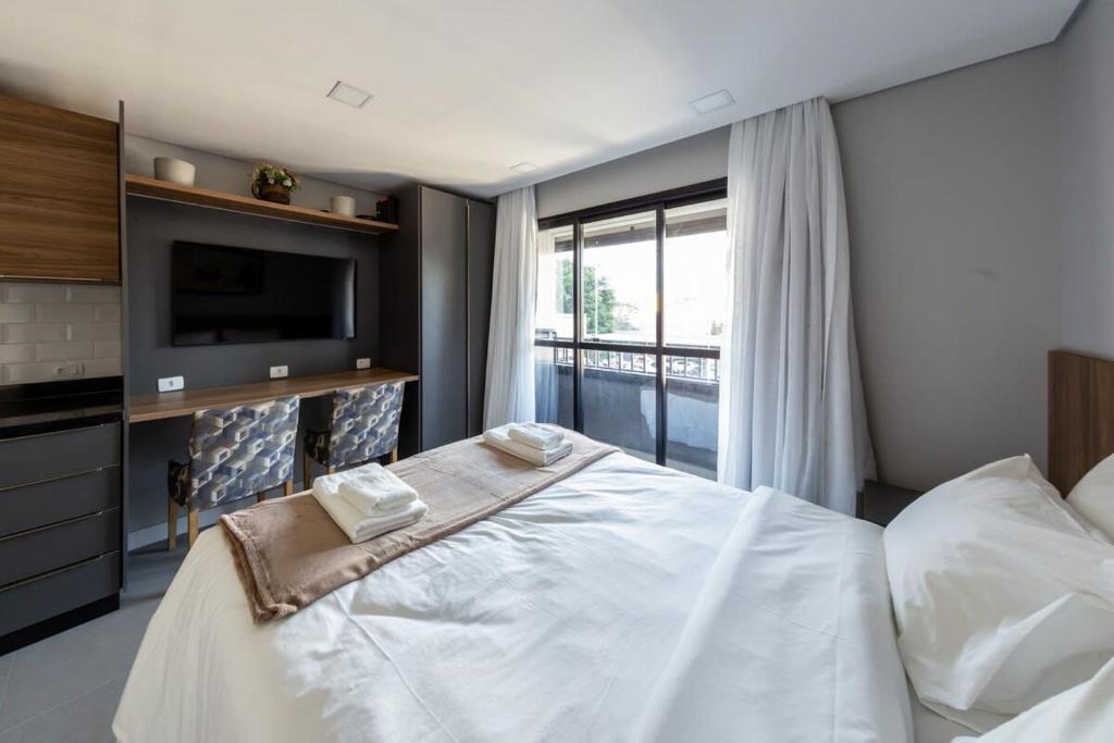 een slaapkamer met een groot wit bed en een televisie bij BHomy Pinheiros - 700m do metrô F Lima RIZ216 in Sao Paulo