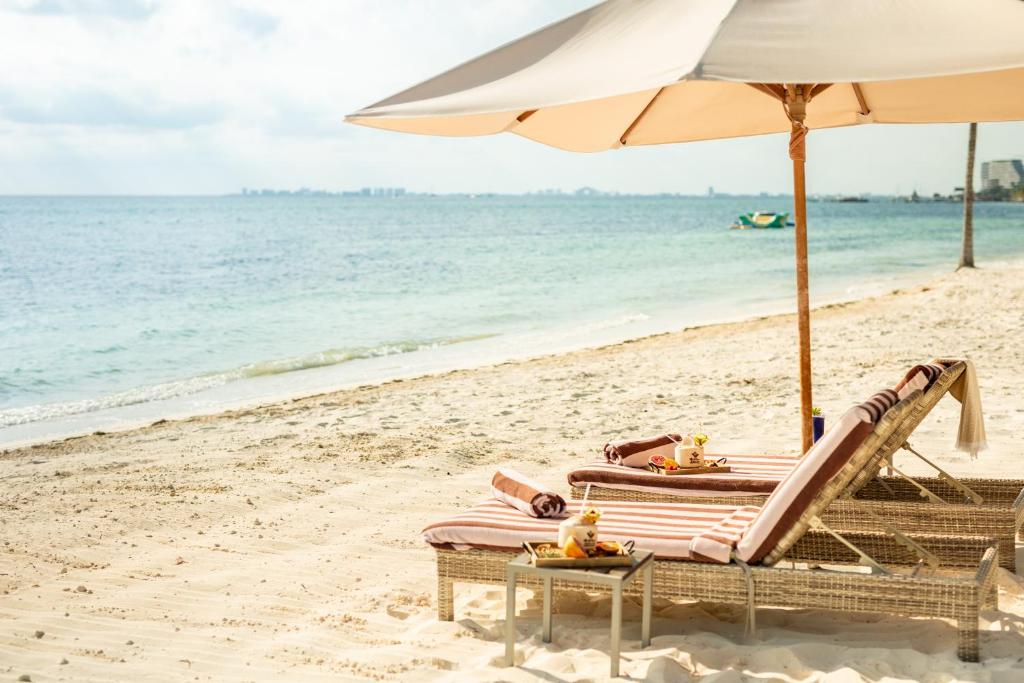 a beach with two lounge chairs and an umbrella at Villa del Palmar Cancun Luxury Beach Resort & Spa in Cancún