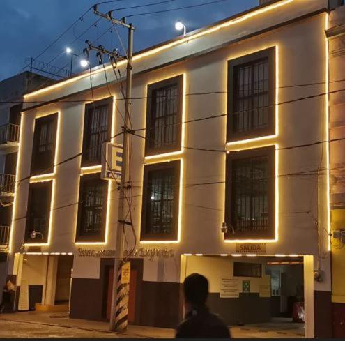 Ein Mann, der an einem weißen Gebäude vorbeigeht, mit Lichtern drauf. in der Unterkunft HOTEL MAQUIAVELO SOLO ADULTOS in Puebla