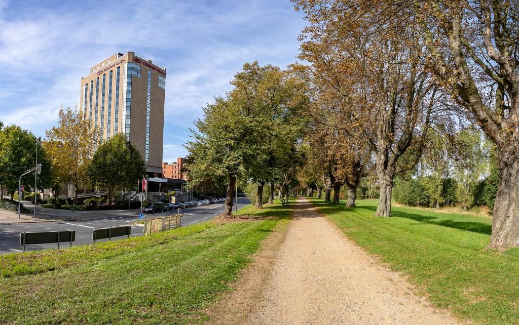 eine unbefestigte Straße in einem Park mit Bäumen und einem hohen Gebäude in der Unterkunft Crowne Plaza Düsseldorf - Neuss, ein IHG Hotel in Neuss