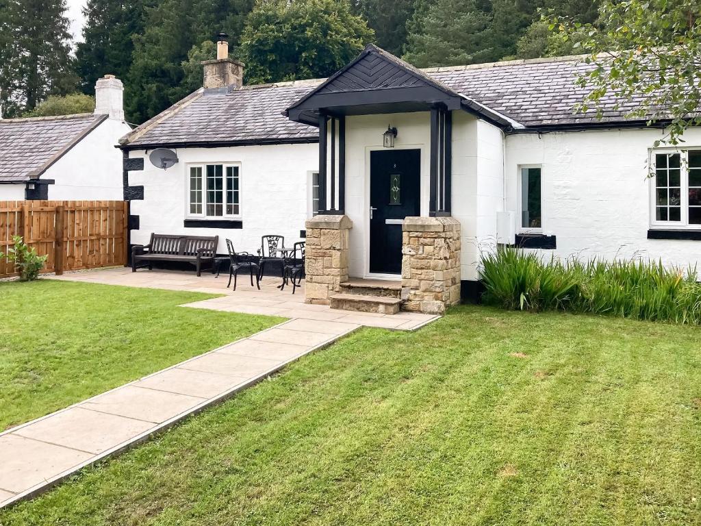 una casa blanca con una puerta negra y un patio en Old Kielder Castle Cottage en Kielder