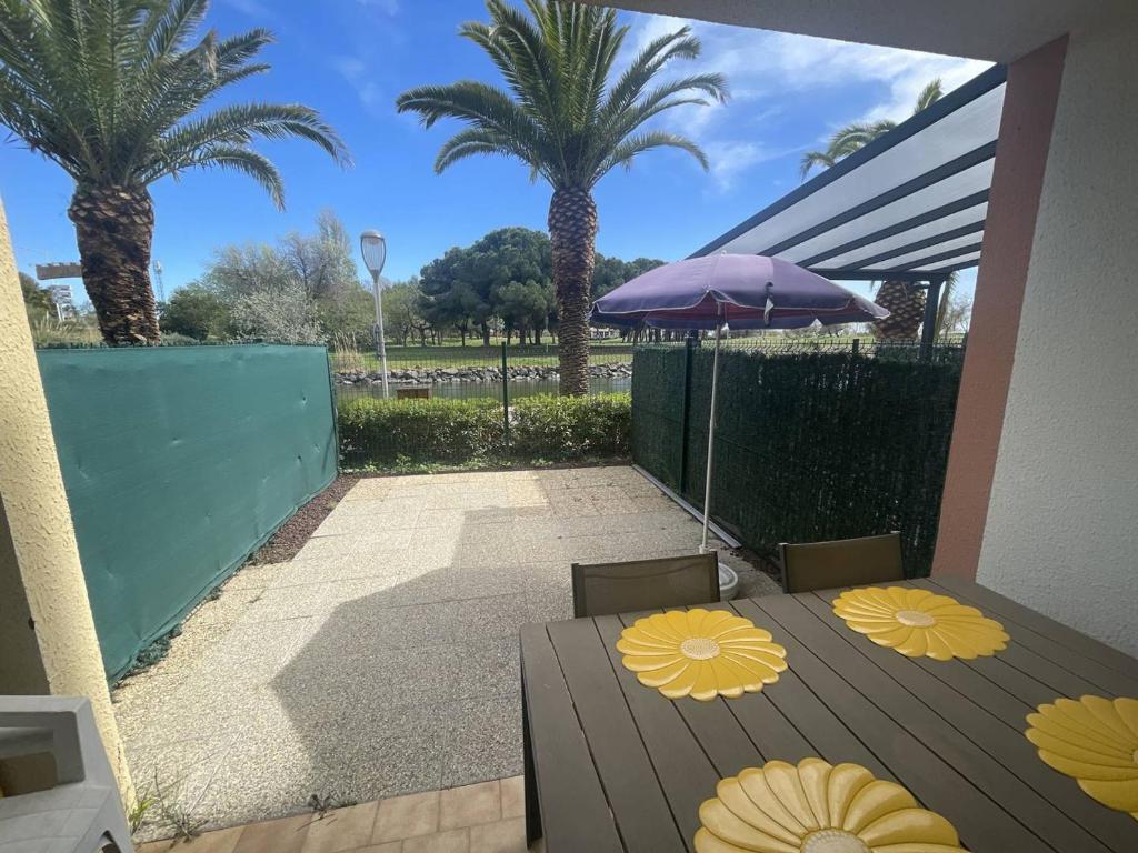 d'une terrasse avec une table, un parasol et des palmiers. dans l'établissement Studio clim proche plage Richelieu, parking - FR-1-723-150, au Cap d'Agde