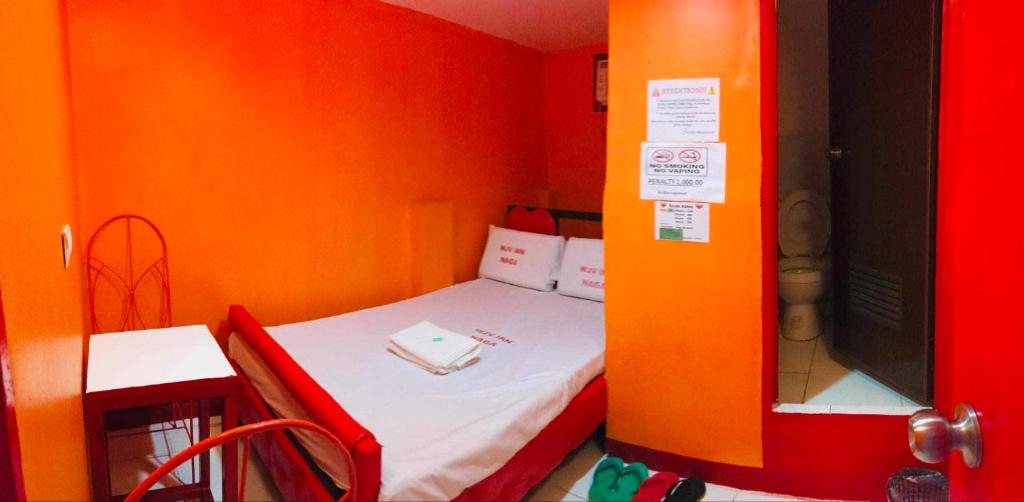 a small room with a small bed with an orange wall at WJV INN NAGA in Tina-an