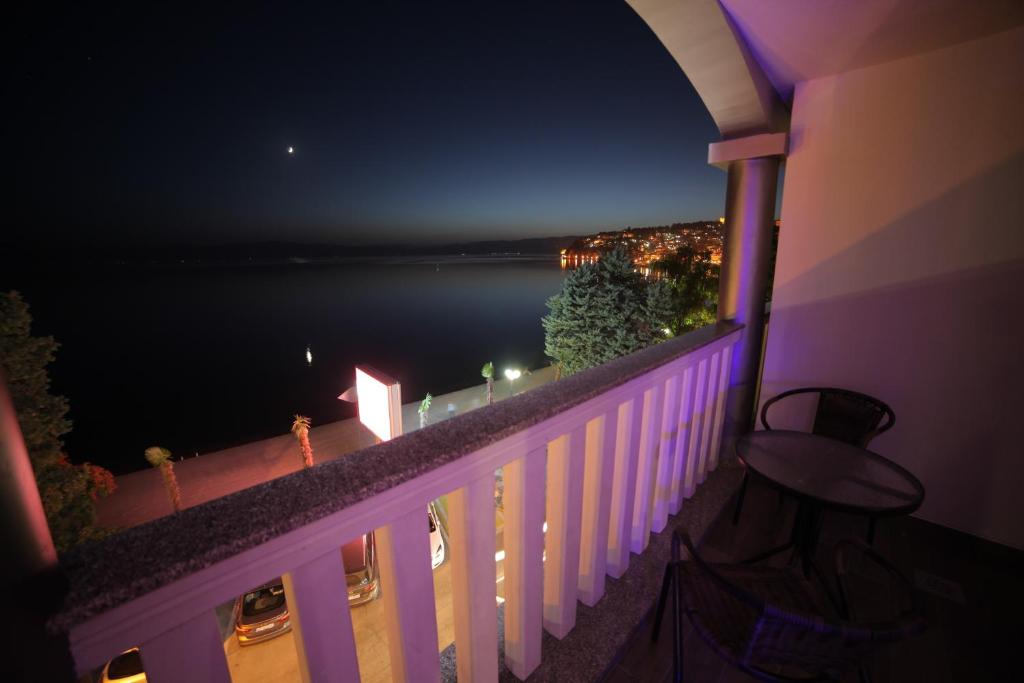 Balcony with table and chairs overlooking moonlit bay, distant coastal town and lit hillside, lit by purple LED column at City Palace Hotel in Ohrid