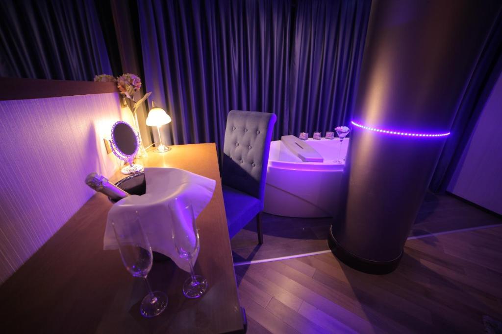 Room with desk and mirror, two wine glasses on a white cloth, upholstered chair and jetted bathtub with purple LED light at City Palace Hotel in Ohrid