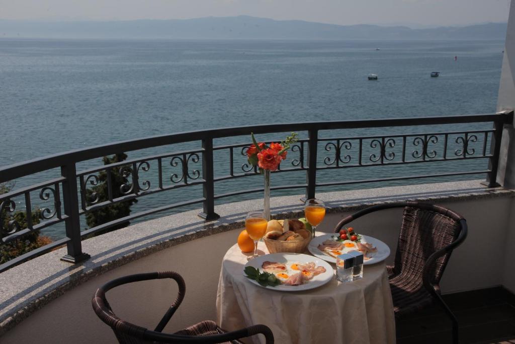 Balcony breakfast with wicker chairs, fruit basket, cold cuts and orange juice overlooking the sea and distant boats at City Palace Hotel in Ohrid