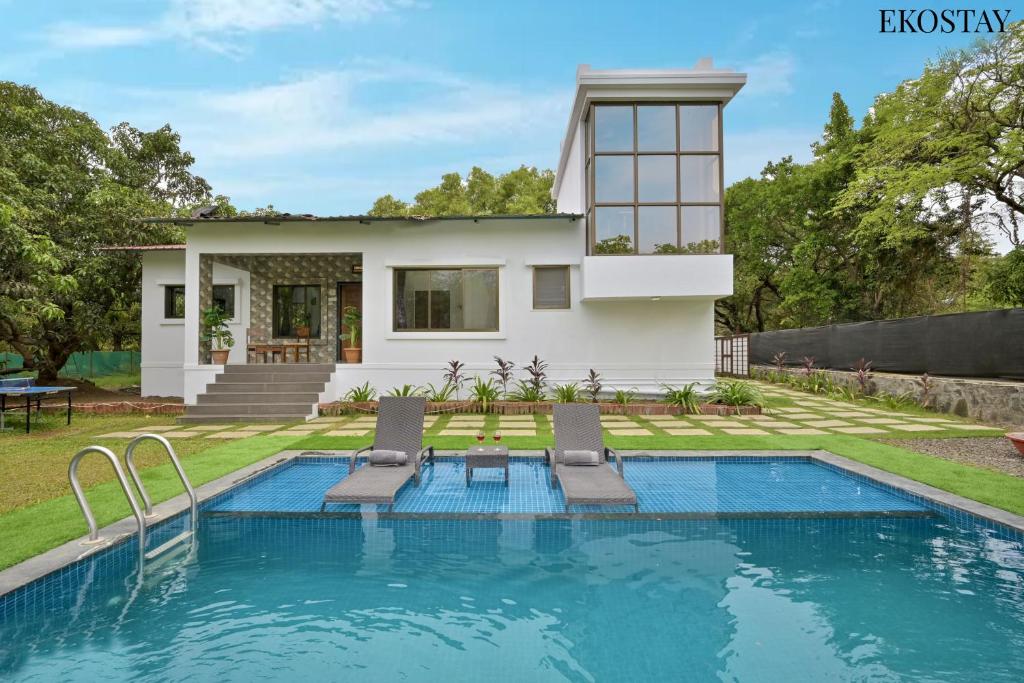 a villa with a swimming pool in front of a house at EKOSTAY - Forestwood Villa in Alibaug